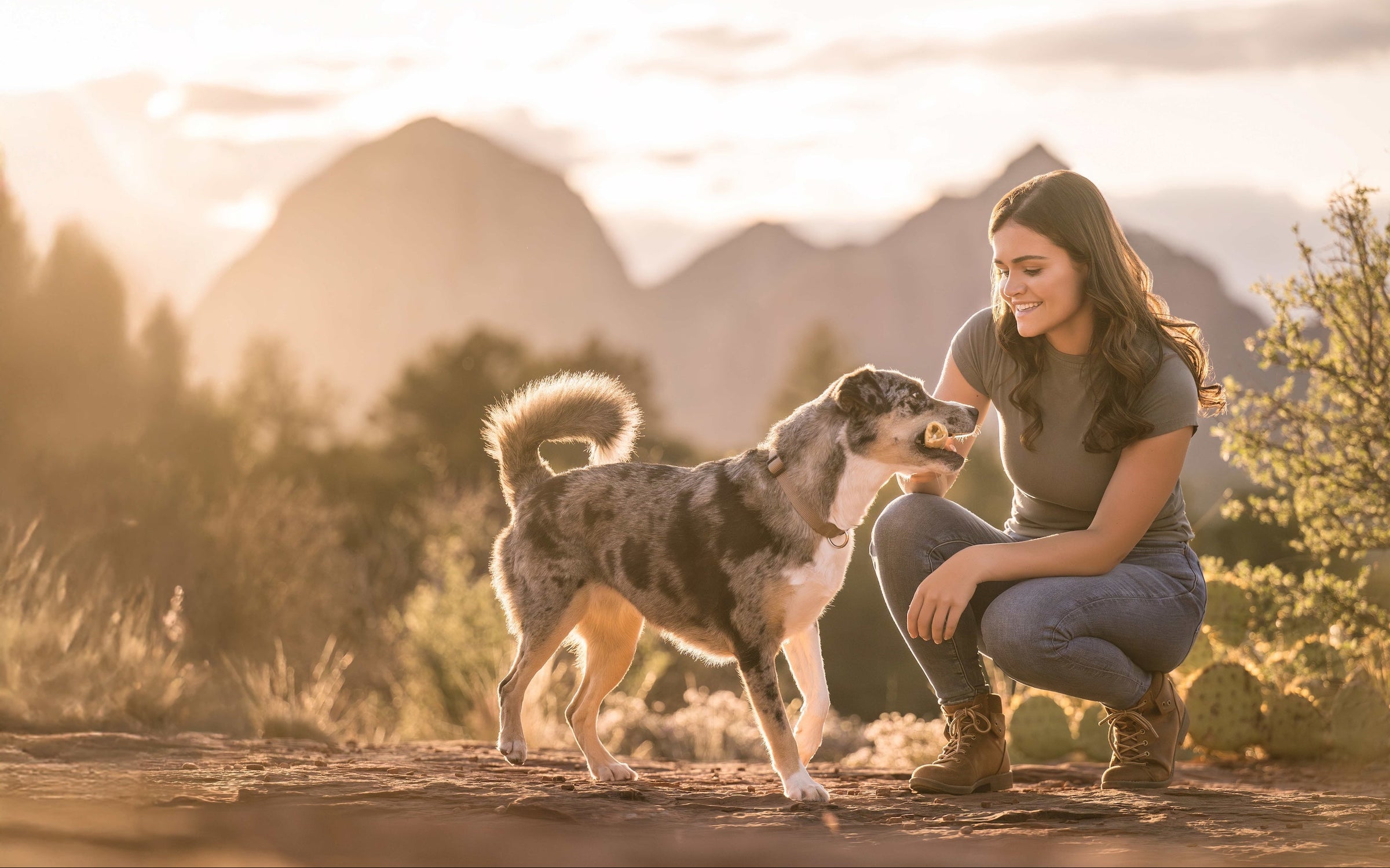 Woman feeding her dog a No-Hide Roll in a natural setting with mountains in the background.