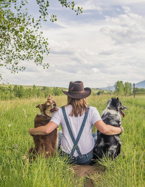 woman sitting in a field with two dogs